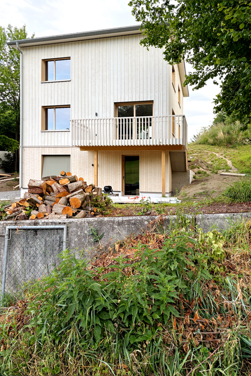 Die neue Gebäudehülle ist eine wärmegedämmte Holzfassade und ein neuer Balkon aus Holz, welcher den alten maroden Betonbalkon ersetzt. Die sägerauen Fassadenbretter wurden mit Schwedenfarbe in Stockholmweiss geschlämmt, Falu Vapen, Holzbau Roger Gassmann Embrach, Bauleitung Nina Wick