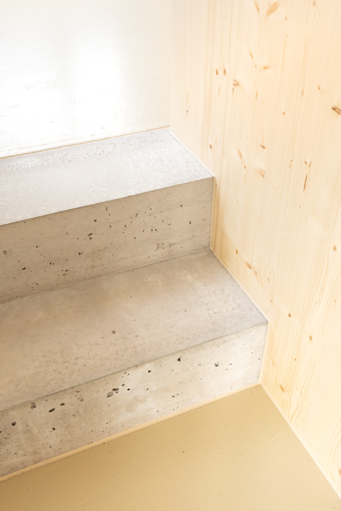 Detailfoto Tieferlegung Bodenplatte mit zwei neuen Treppenstufen aus Sichtbeton, Anhydrit Gussboden und Fichtenholz Einbauten.